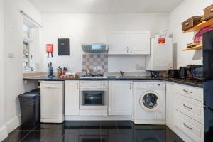 cocina con armarios blancos, lavadora y secadora en Modern Living in the Heart of Covent Garden! 6BC en Londres