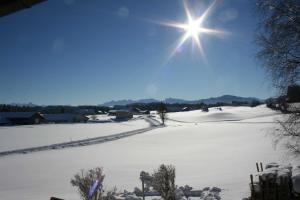 un campo cubierto de nieve con el sol en el cielo en Haus Allgäu Ruh, en Görisried