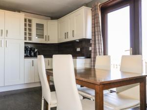 cocina con mesa de madera y sillas blancas en Hidden House Hebrides, en Garrabost