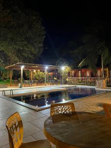 a swimming pool at night with a table and chairs at Pousada Ilha do Meio in Itacimirim