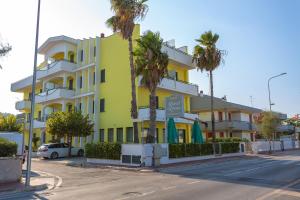 un bâtiment jaune et blanc dans une rue bordée de palmiers dans l'établissement Hotel Roma Sul Mare, à Roseto degli Abruzzi