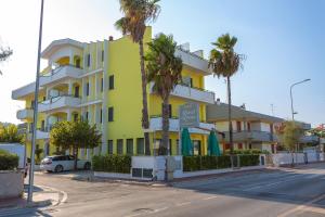 a yellow and white building on a street with palm trees at Hotel Roma Sul Mare in Roseto degli Abruzzi