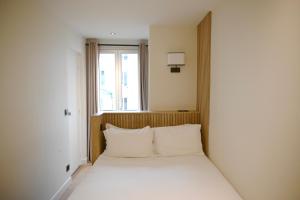 Cette chambre comprend un lit avec des oreillers blancs et une fenêtre. dans l'établissement Pavillon de Montmartre, à Paris