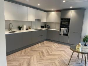 a kitchen with white cabinets and a wooden floor at Modern Raynes Park Apartment x2 Bathroom*Garden*Wifi* in Raynes Park