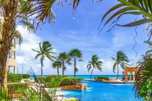 a view of a pool with palm trees and the ocean at Oceanfront Condo a Block Off 5th in Heart of Playa in Playa del Carmen +21 photos