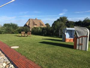 a yard with a thatched building and a playground at Pension Sössaarep's Hüs in Nebel +19 photos