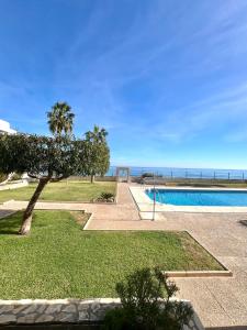 a swimming pool with a palm tree and the ocean at Apartamento Las Olas in La Marina de la Torre