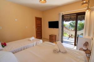 a bedroom with two beds and a tv and a window at Pousada Morro do Caburé in Cajueiro