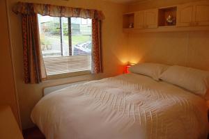a bedroom with a white bed and a window at Caravan B26 at The Woodlands in Tywyn
