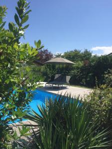 a swimming pool with an umbrella and a chair at Maison l'heure bleue in Lanton