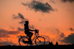 una mujer montando una bicicleta delante de una puesta de sol en Cottage 11 - 1 Bed / 1 Bath w/ Private Courtyard, en Wolfeboro