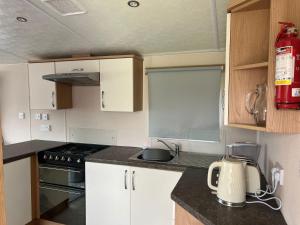a small kitchen with white cabinets and a stove at Lovely Caravan At Lower Hyde Holiday Park, Isle Of Wight Ref 24001g in Shanklin