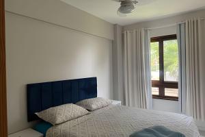 a bedroom with a bed with a blue headboard and a window at Lindo apto no Condomínio Enseada Praia do Forte in Mata de Sao Joao