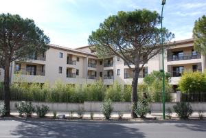 un immeuble d'appartements avec des arbres devant lui dans l'établissement UZES APPART HOTEL Résidence Le Mas des Oliviers, à Uzès