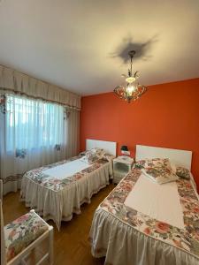 two beds in a room with orange walls and a chandelier at Apartamento Curros Enríquez in Cambados