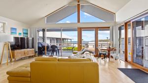 a living room with a yellow couch and a large window at Sheoak Holiday Home in Coffin Bay