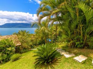 a garden with palm trees and a pathway next to the water at Bangalô Ilhabela in Ilhabela