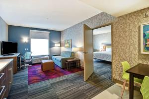 テレホートにあるHome2 Suites By Hilton Terre Hauteのベッドとリビングルームが備わるホテルルームです。