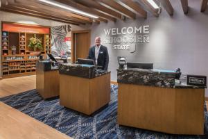 um homem de pé numa mesa de boas-vindas numa loja em Hampton Inn & Suites Fort Wayne Downtown em Fort Wayne