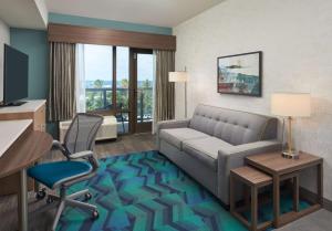 a hotel room with a couch and a desk and chair at Home2 Suites By Hilton Pompano Beach Pier, Fl in Pompano Beach