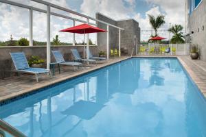 a swimming pool with chairs and umbrellas on a building at Home2 Suites by Hilton Fort Myers Airport in Fort Myers