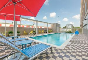 a swimming pool with chairs and a red umbrella at Home2 Suites By Hilton El Campo in El Campo