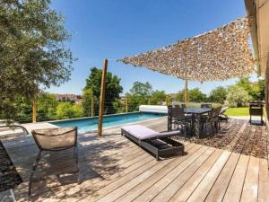 una terrazza in legno con tavolo e sedie accanto alla piscina di Élégante maison à Vichy : piscine chauffée, jardin arboré, terrasse et climatisation - FR-1-489-494 a Vichy