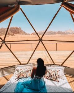 een vrouw op een bed in een tent met uitzicht op de woestijn bij Rum Elegant luxury camp in Wadi Rum