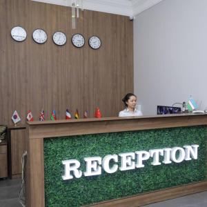 a woman behind a reception desk with clocks on the wall at OA Tashkent in Qŭyliq