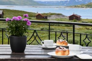 Eidsbugarden的住宿－Tyinholmen Høyfjellsstuer，木桌上带咖啡杯的2份盘子糕点