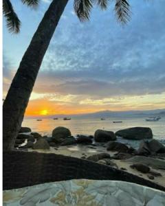 zachód słońca na plaży z palmą i oceanem w obiekcie Encanto do Mar w mieście Praia de Araçatiba
