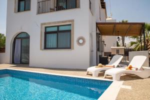uma villa com uma piscina e 2 cadeiras brancas em Oceans Breeze Villa em Protaras