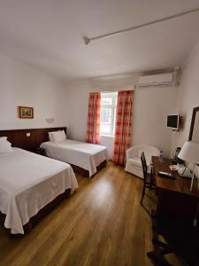a hotel room with two beds and a desk at Hotel Beira Mar in Angra do Heroísmo