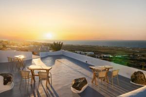 a rooftop patio with tables and chairs and the sunset at Sun Angelos Oia - Luxury Cave Suites in Oia