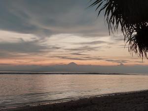 a sunset on the beach with a mountain in the background at Sahara Sands Guest House - Gili Trawangan in Gili Trawangan