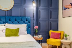 Dormitorio azul con cama y silla amarilla en Regency Basement Apartment en Cheltenham