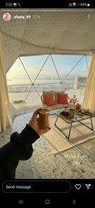 a person holding a cup of coffee in front of a tent at AVICENNIA BEACH DOMES in Salalah