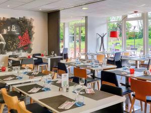 a dining room with tables and chairs and windows at Novotel Saclay in Saclay