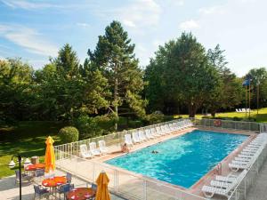 a large swimming pool with chairs and tables and umbrellas at Novotel Saclay in Saclay