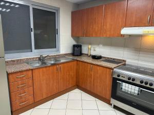 eine Küche mit Holzschränken, einem Waschbecken und einem Fenster in der Unterkunft Luxury Apartment 2 BR Al Majaz 2 view in Schardscha