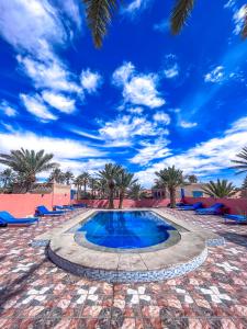 a swimming pool with palm trees and a blue sky at Riad Les Roches Merzouga in Merzouga