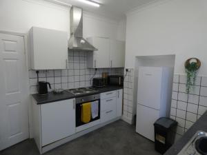 a kitchen with white cabinets and a stove and refrigerator at Comfy 3 Bedroom Cottage in a Calm Location in Abertillery