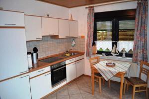 - une cuisine avec des placards blancs, une table, une table et des chaises dans l'établissement Ferienwohnung Gartenweg, à Carolinensiel
