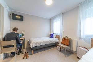 a man is sitting at a desk in a bedroom at Montempô Apparthôtel Lyon Viviani in Vénissieux