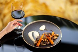 a person holding a glass of wine next to a plate of food at Aria Hotel Budapest by Library Hotel Collection in Budapest