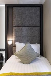 a bed with a large headboard and a pillow on it at Mornington Hotel London Victoria in London