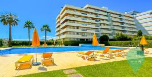 a pool with chairs and umbrellas next to a building at Vista dos Seus Sonhos T2 HsR Vilamarina in Quarteira