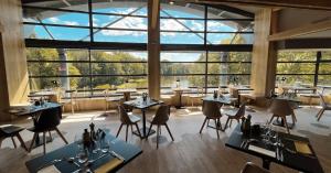 een restaurant met tafels en stoelen en een groot raam bij Le Forges Hotel in Forges-les-Eaux