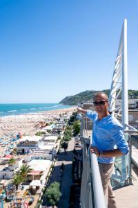 um homem de pé numa varanda com vista para uma praia em Hotel Thea & Residence em Gabicce Mare