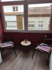 twee stoelen en een tafel in een kamer met twee ramen bij Lembranzas in Padrón